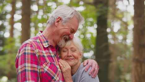 loving retired senior couple hugging on walk in woodland countryside together