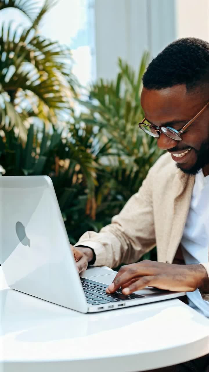A candid video captures a man typing on a laptop in a lush indoor setting