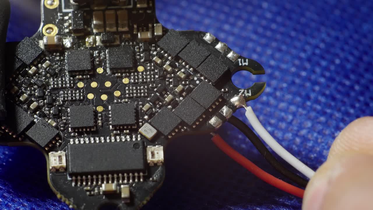 SLOW MOTION CLOSE UP OF A MAN SOLDERING A WITHE CABLE TO A ALL-IN-ONE FPV FLIGHT CONTROLLER