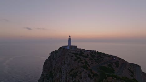 Retroceso-Aéreo-Mientras-El-Cielo-Del-Atardecer-Rodea-El-Faro-De-Formentor,-Serra-De-Tramuntana-Mallorca-España-Mientras-El-Coche-Sube