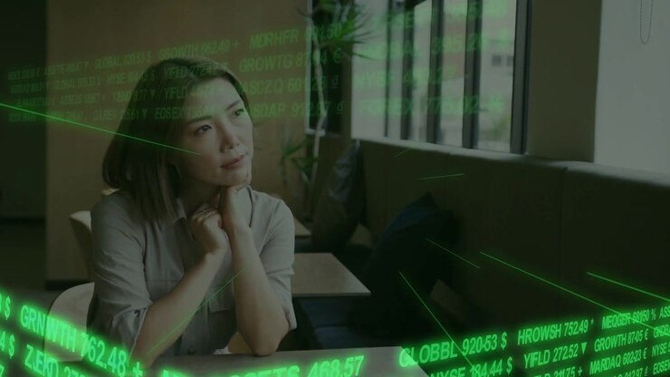 Reacting to ticker, Asian woman wearing blouse following numbers at table by window tracking stocks
