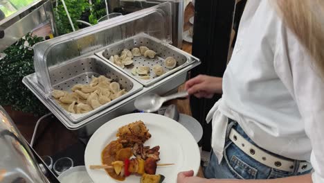 woman serving herself at a buffet with dumplings and other dishes