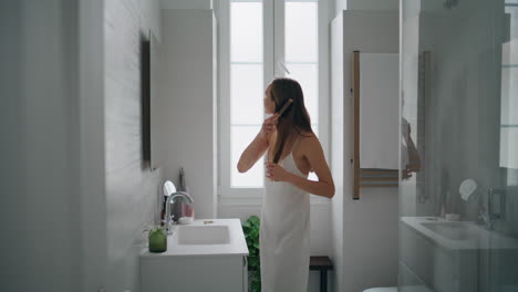 Attractive-model-combing-hair-at-mirror-place.-Woman-doing-hairstyle-in-bathroom