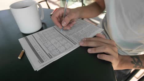 a person works on a newspaper puzzle while smoking and drink coffee