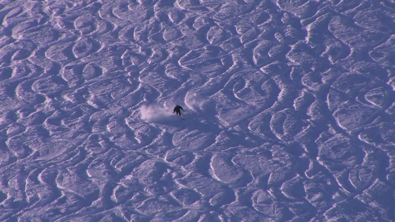 un esquiador se dirige por una amplia pendiente de senderos y moguls