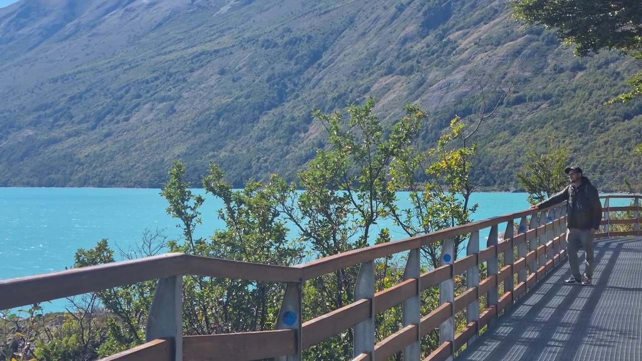 Escursionista in piedi su una passerella di legno accanto al Lago Argentino dopo aver visitato il Ghiacciaio Perito Moreno, che ammira il panorama mozzafiato di acque turchesi e aspre montagne patagoniche