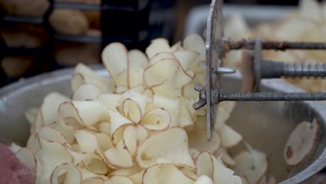 primer plano de cintas de patatas rizadas saliendo de un cortador de tornado