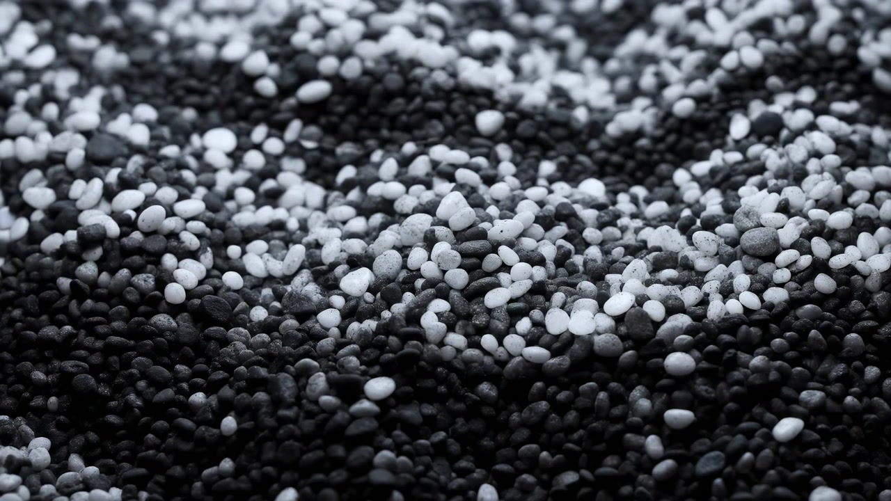 Dense rounded pebbles cover entire view in black gray and white tones with rough granular texture soft