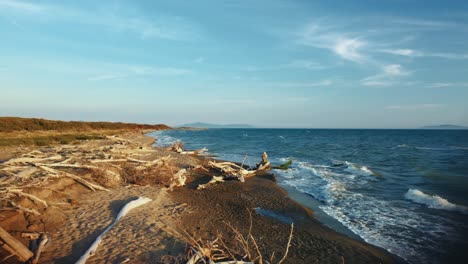aerial drone footage flying back from a sandy sunset beach at the seaside near castiglione in the iconic maremma nature park in tuscany, italy, with waves, islands and a cinematic dramatic red sky