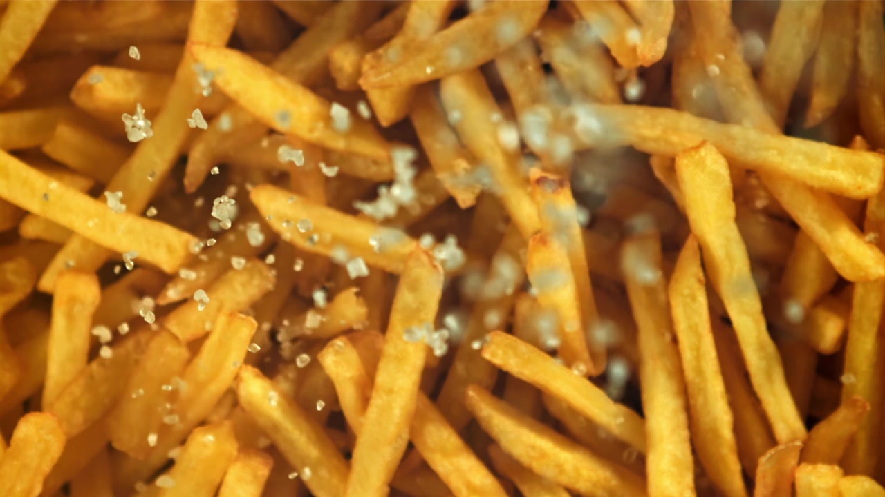 Primer plano de cristales de sal cayendo sobre patatas fritas doradas