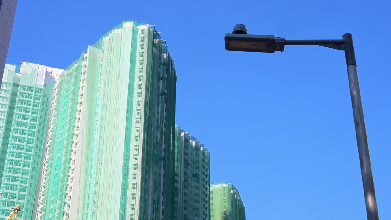 Residential skyscrapers undergo renovation covered in green protective netting in Hong Kong. Establishing shot of urban renewal, building maintenance, and real estate development in China.
