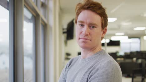 Portrait-of-caucasian-creative-businessman-standing-at-window,-looking-at-camera-and-smiling