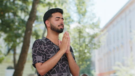 indian man tourist praying with closed eyes to god asking for blessing help forgiveness outdoors