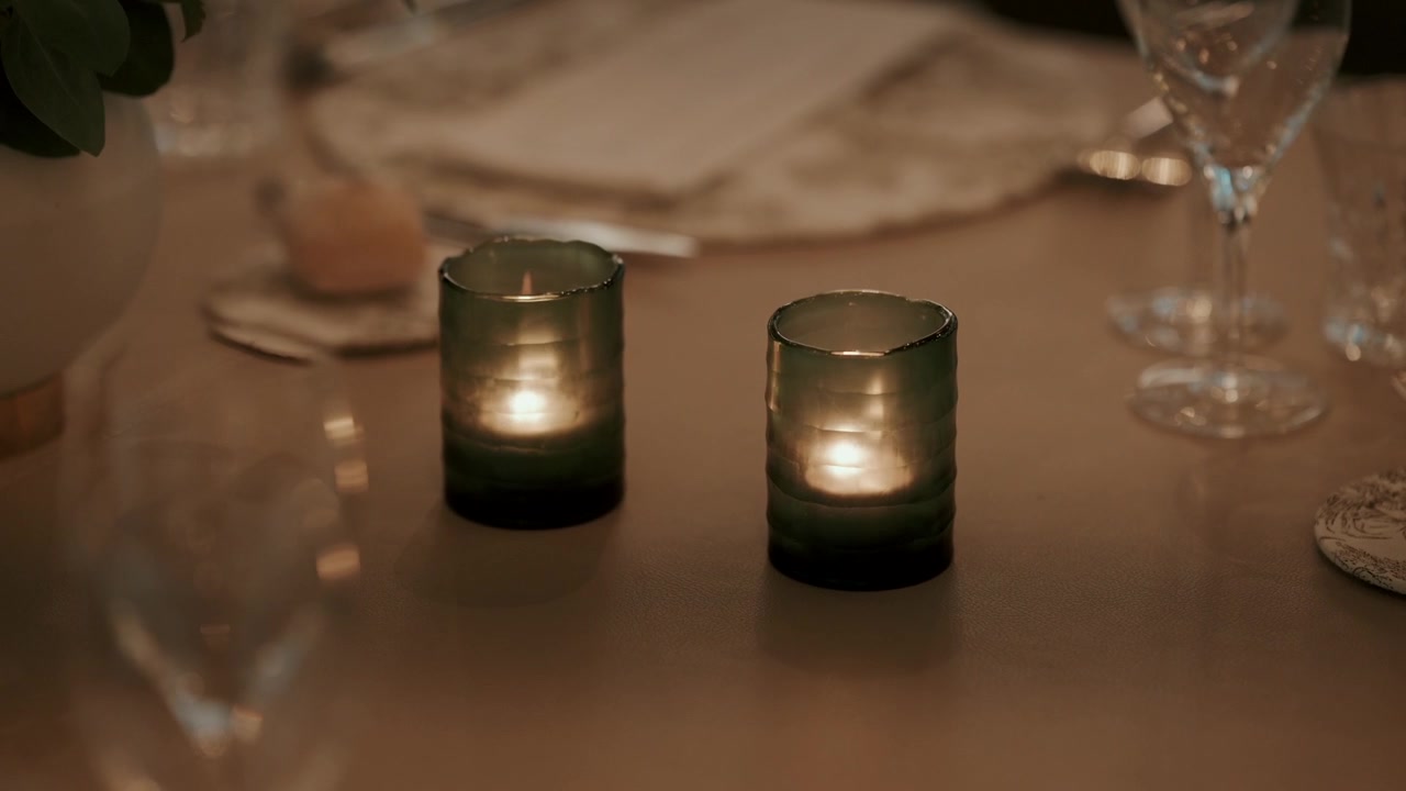 Paire de bougies votives en verre vert allumées projetant une lumière chaude sur une table de banquet dressée la nuit.