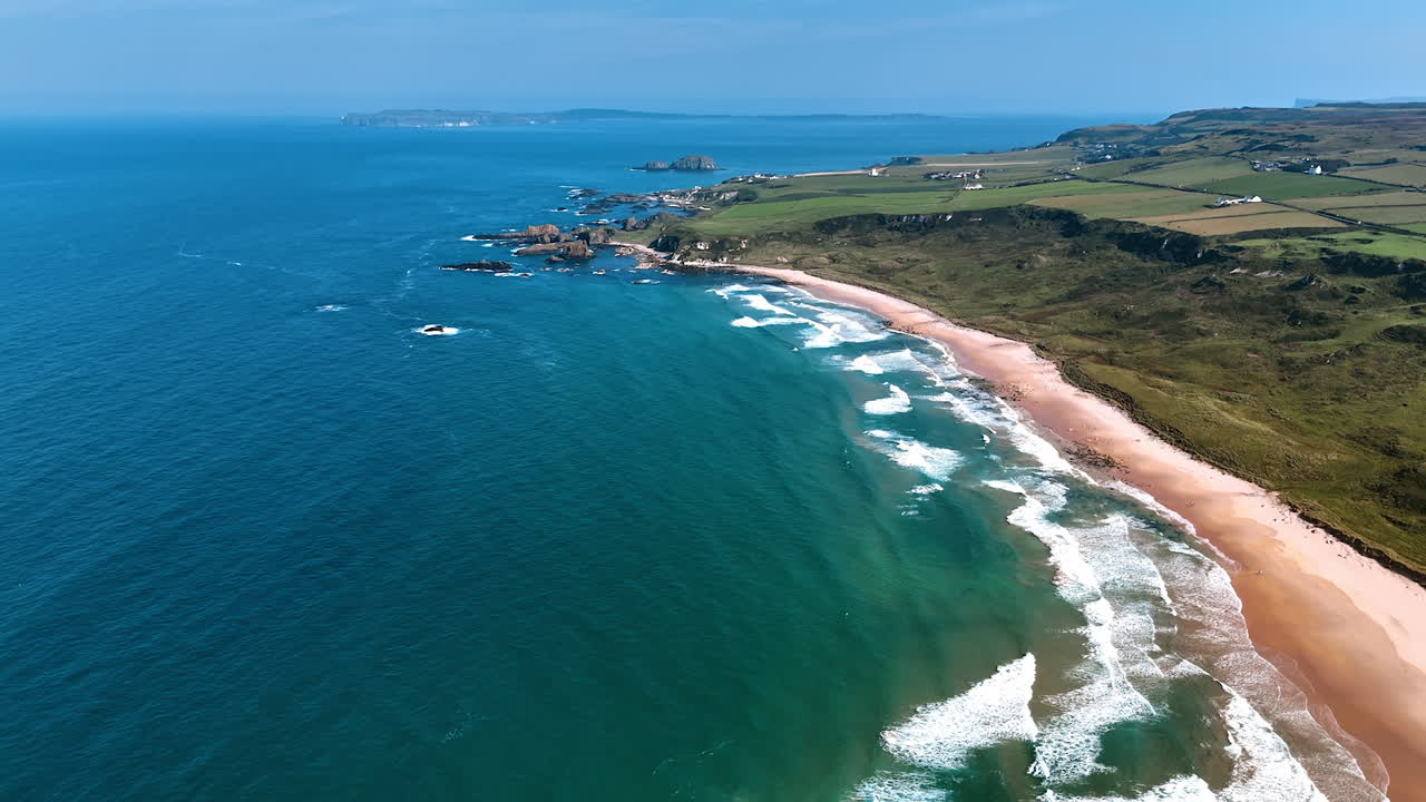 Picturesque green shore of Ireland. Drone footage above the waterscape of the Atlantic Ocean at the coast with narrow sandy beach. Aerial view.