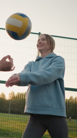 un principiante de voleibol recibe entrenamiento del entrenador en una cancha al aire libre, el jugador pierde la pelota durante la sesión de práctica, ambos se ríen y sonríen, el entrenador se mueve para recuperar la bola durante una sesión de entrenamiento