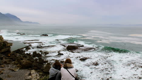 Two-young-women-sitting-on-cliff-lookout-point