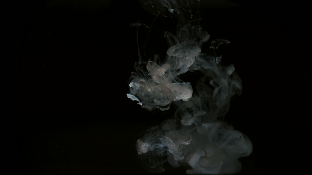 흰색 잉크 방울은 어두운 액체에 잠기고 용해됩니다.