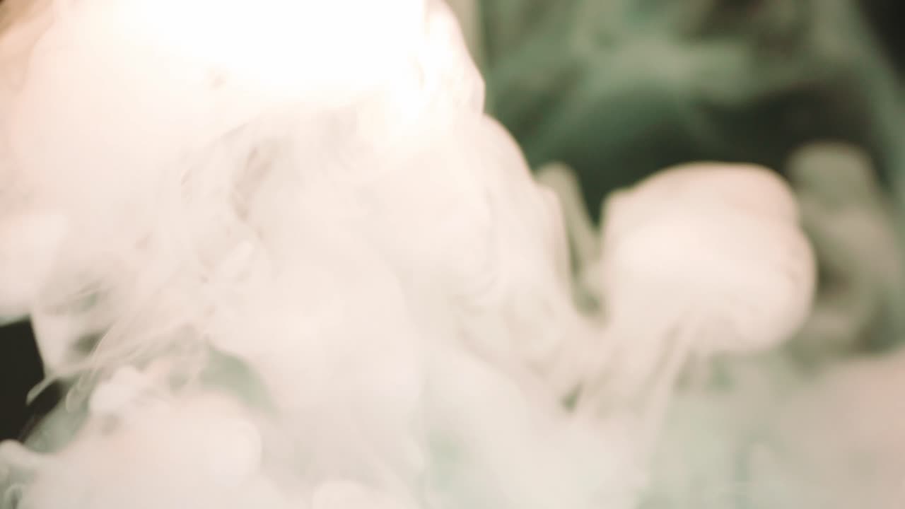 초록색과 오렌지색 연기의 추상적인 움직임, 어두운 배경의 증기와 빛이 그 위에 떨어집니다.