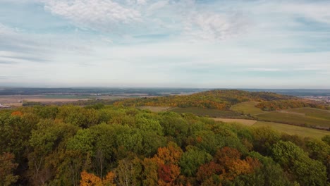 flying over an autumnal forest on a hill with fields and villages in the background