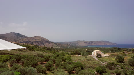 sobrevuelo aéreo bajo del lujoso patio de la villa griega, tumbonas y follaje que revelan la costa a lo lejos en creta, grecia