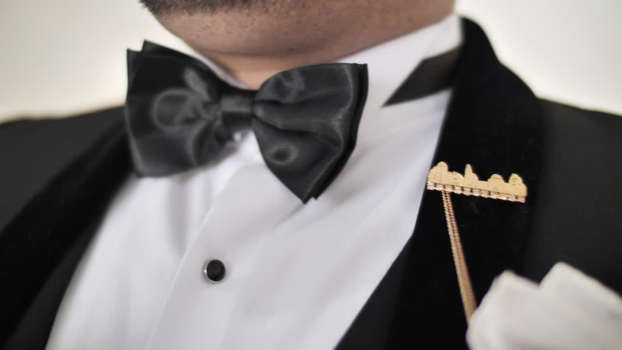 Man in formal elegant suit fastening black bow tie, close up on hands, arc shot