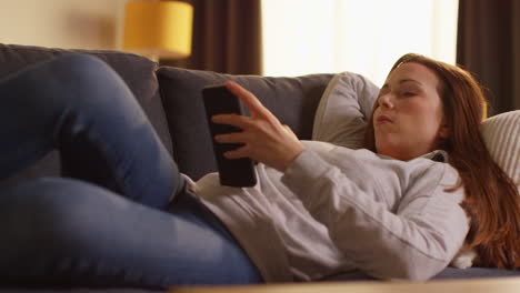 Close-Up-Of-Woman-Lying-On-Sofa-At-Home-At-Streaming-Or-Watching-Movie-Or-Show-Or-Scrolling-Internet-On-Mobile-Phone-2