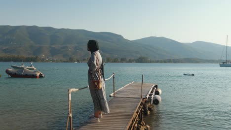 beautiful young moroccan woman standing on jetty admiring seaside view