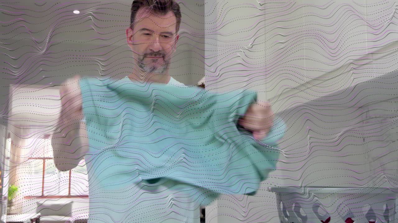 Man pulling from basket coral and teal tops, inspecting, smoothing, folding on counter for laundry