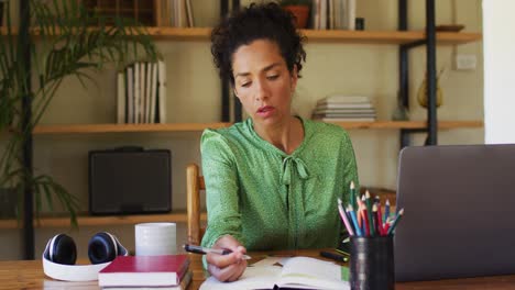 Mixed-race-woman-taking-notes-while-working-from-home