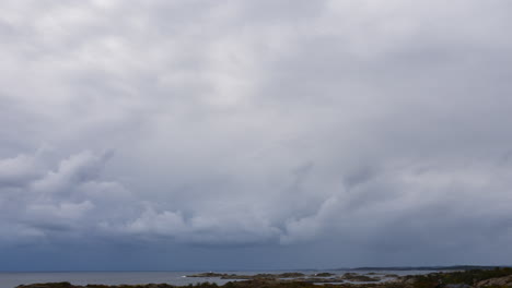 Dark-Blue-Grey-Clouds-Roll-in-Over-Tranquil-Coastal-Landscape,-Stormy-Cloudscape