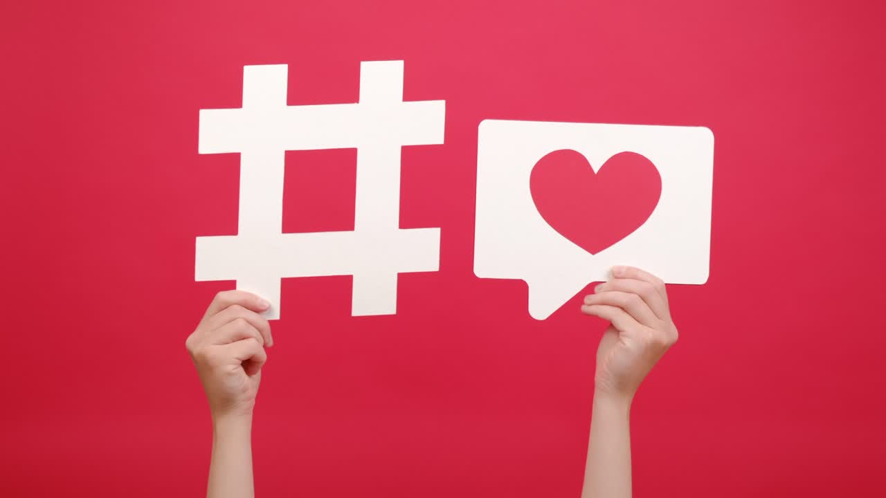 Female hands holding big white hashtag sign and heart icon, posing isolated over red color background in studio with copy space, symbol of charity on Internet. Education, technology, online concept