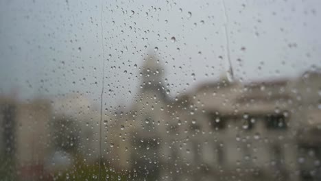 una vista de primer plano en cámara lenta de las gotas de lluvia vistas a través de una ventana durante las fuertes lluvias, con un paisaje urbano en el fondo