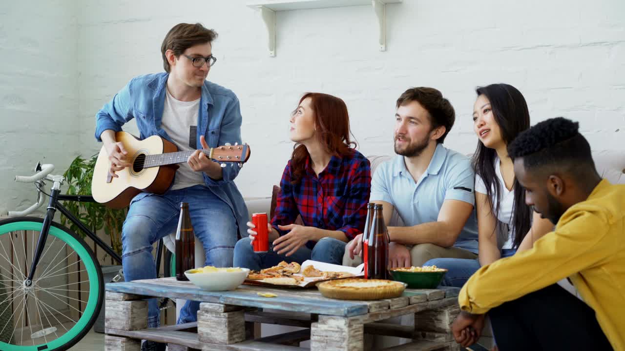jóvenes amigos felices tienen una fiesta tocando la guitarra y cantando juntos en casa