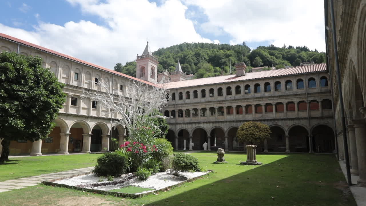 Historic monastery courtyard with arches and lush greenery under a partly cloudy sky