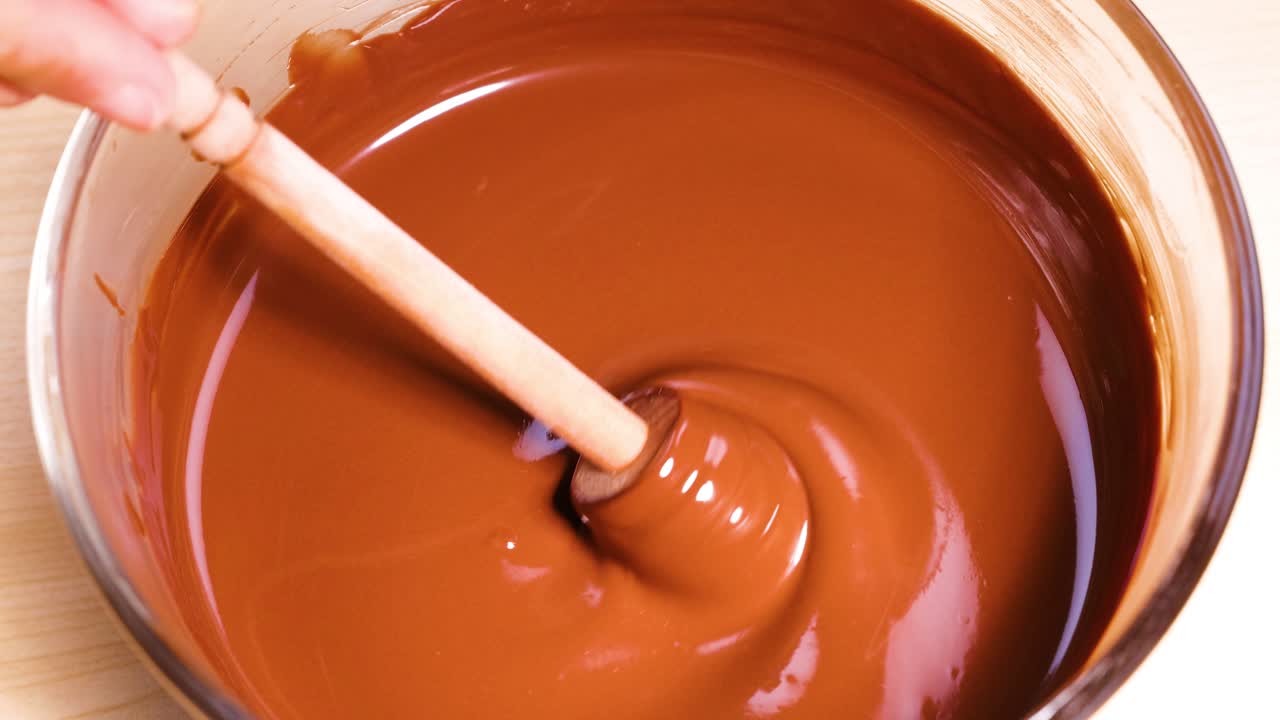 Mano che mescola il cioccolato con un cucchiaio di legno