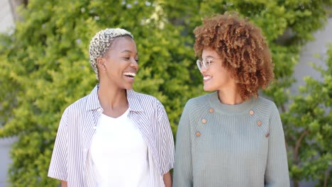 Portrait-of-happy-diverse-female-lesbian-couple-looking-at-camera-in-garden-in-slow-motion