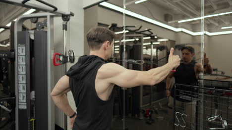 fitness trainer man training rear deltoid performing rear delt cable fly exercise standing in front of mirror