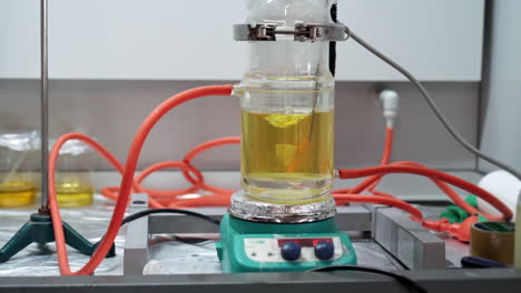 twisting motion of mechanical stirrer with yellow liquid in glass beaker on hot plate in scientific chemical laboratory in slowmo