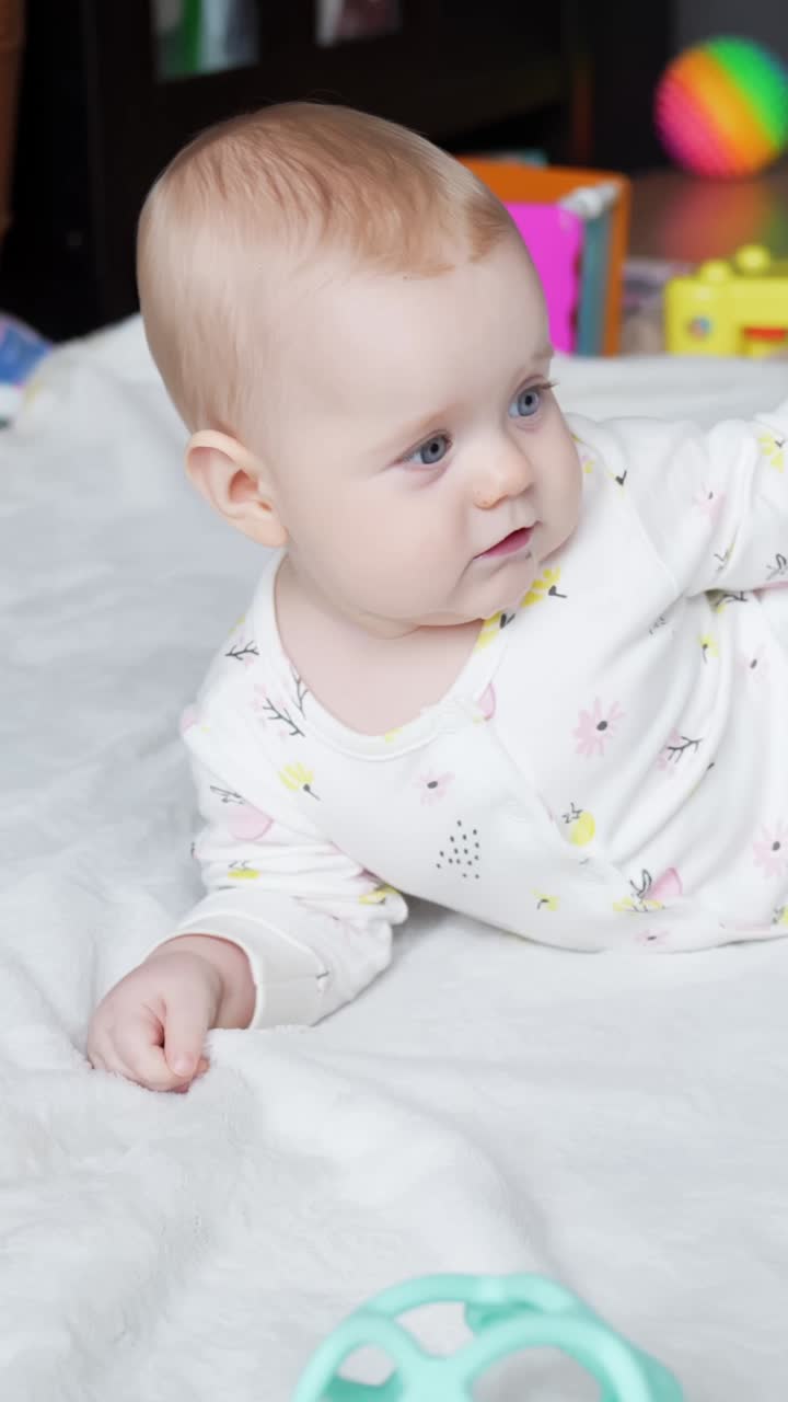 Baby girl lying down playing gently with colorful toys while smiling and exploring on a blanket, pulling at fluff
