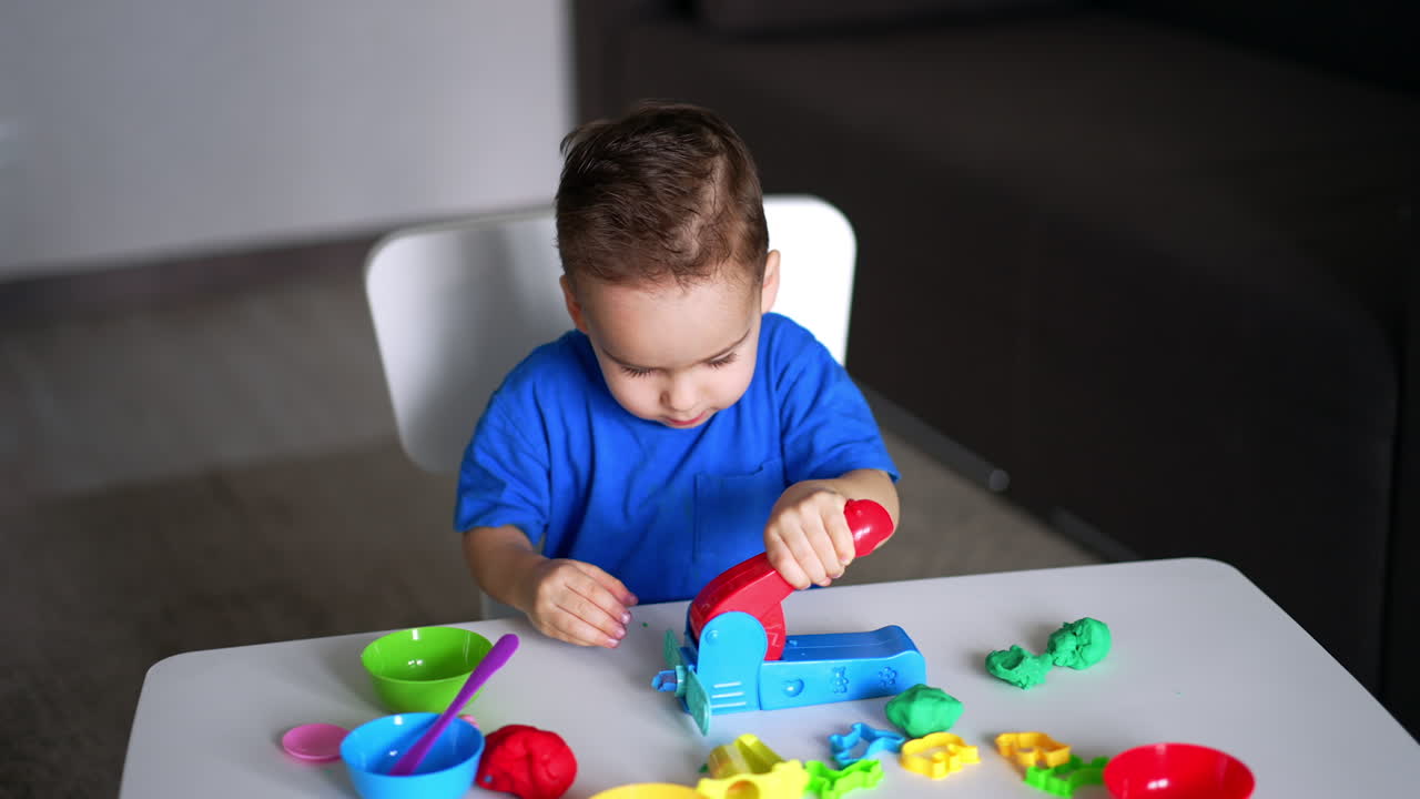 Adorable baby boy uses special device for plasticine sculpturing. Cute toddler playing at home.