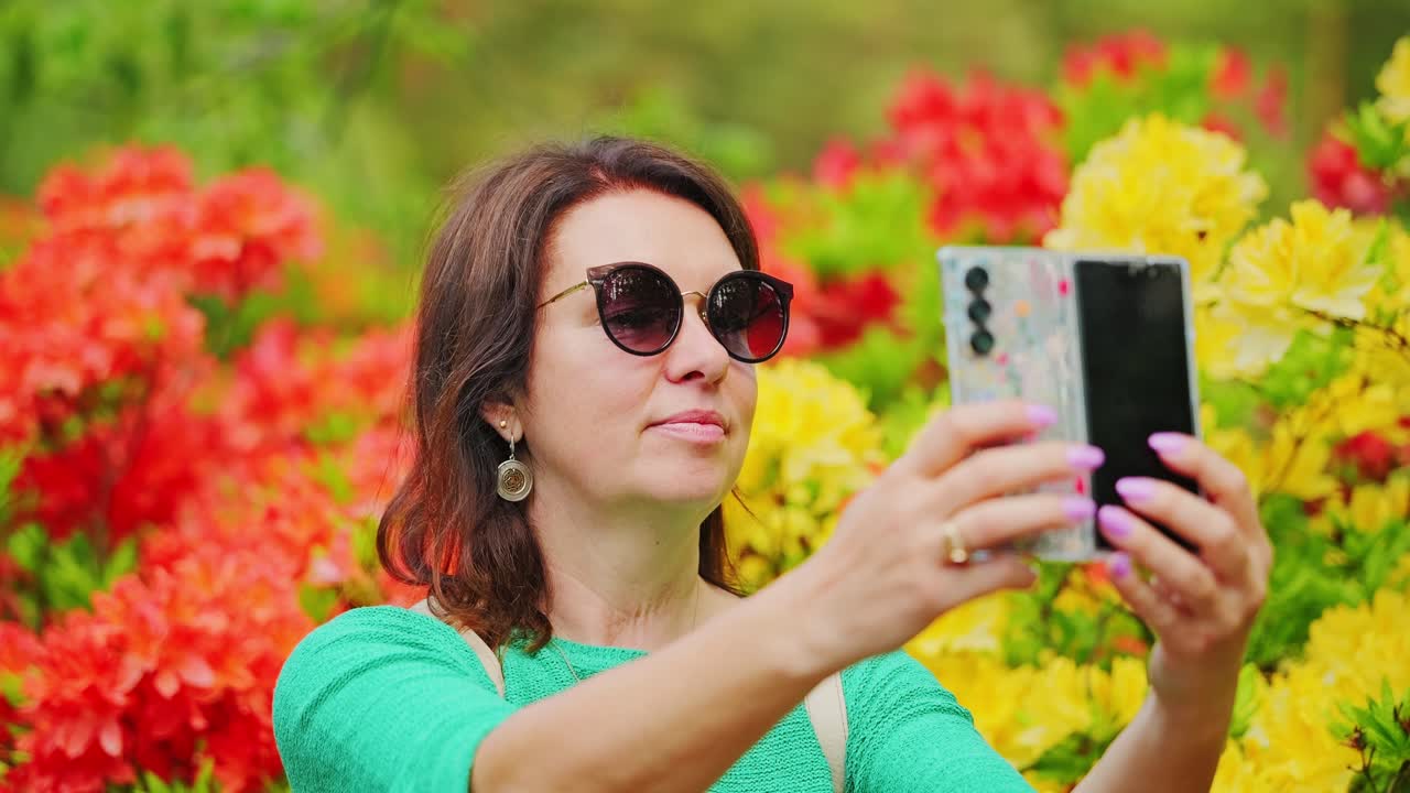 Mulher elegante usa smartphone dobrável entre rododendros floridos, hora da selfie