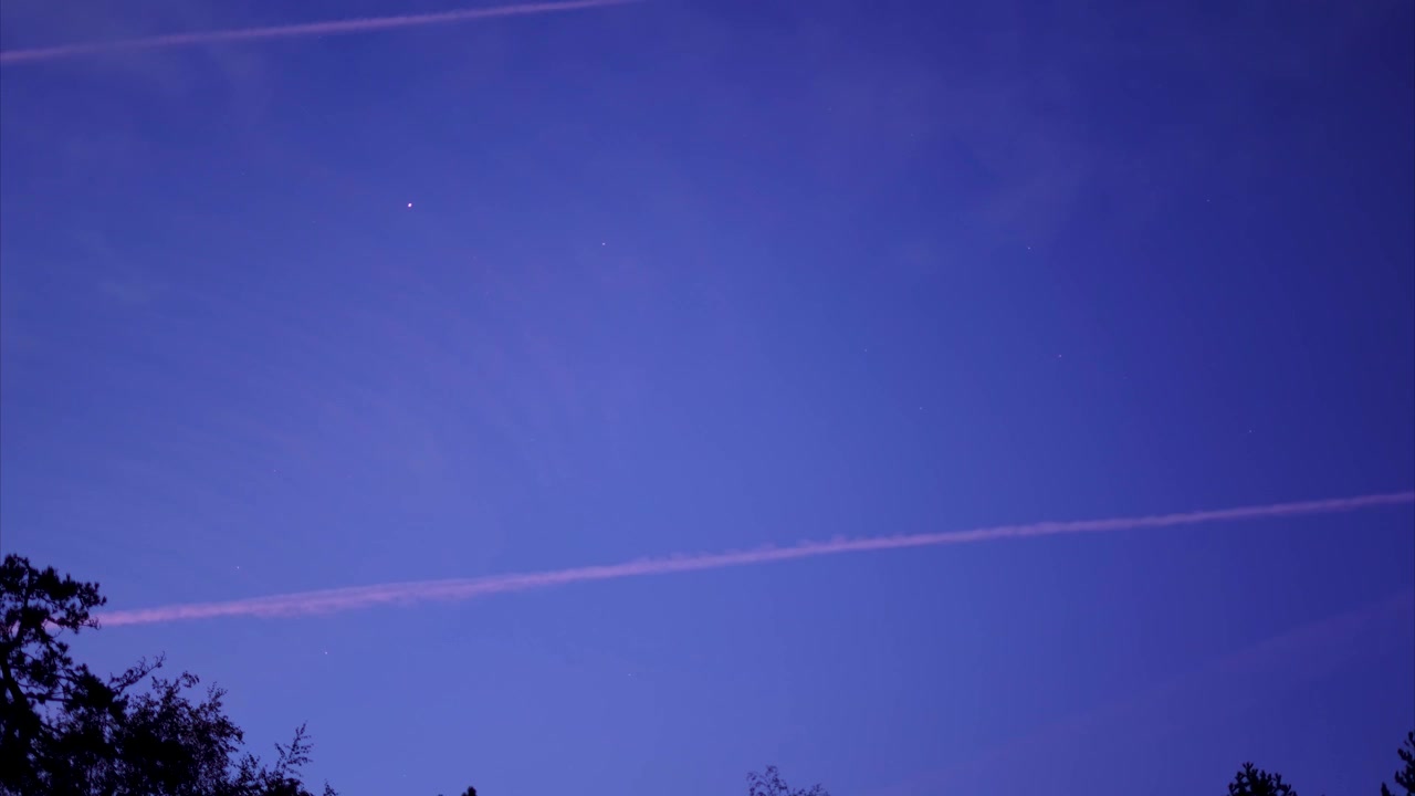 Timelapse 4K dalla notte al giorno, con scie di condensazione di aerei che si susseguono nel cielo scuro.