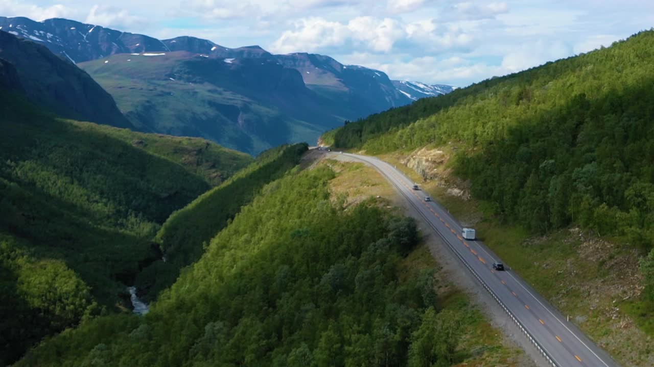 Drone shot following cars and a caravan, driving on a alpine road, Boreal mountains in the background, sunny day, in Northern Norway - rising, aerial view