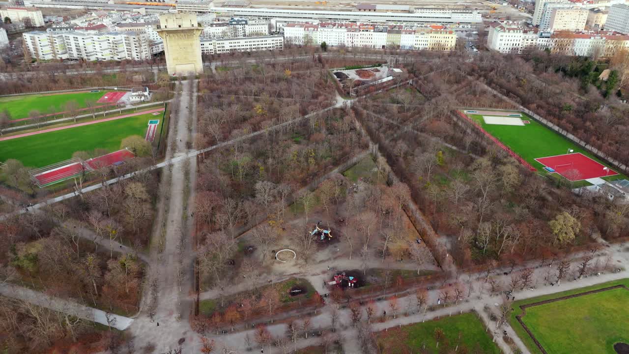 Аэросъемка парка Ауgarten в Вене на закате зимой: панорамный вид с дрона на голые деревья, территорию парка, окружающие городские здания и теплый солнечный свет, освещающий зимний городской пейзаж