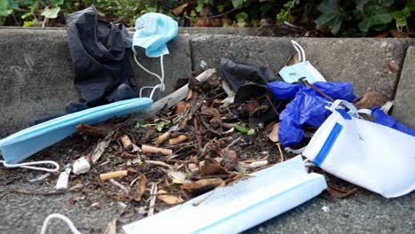 dirty disposable corona virus face masks and latex gloves among cigarette rubbish on street curb pavement dolly right