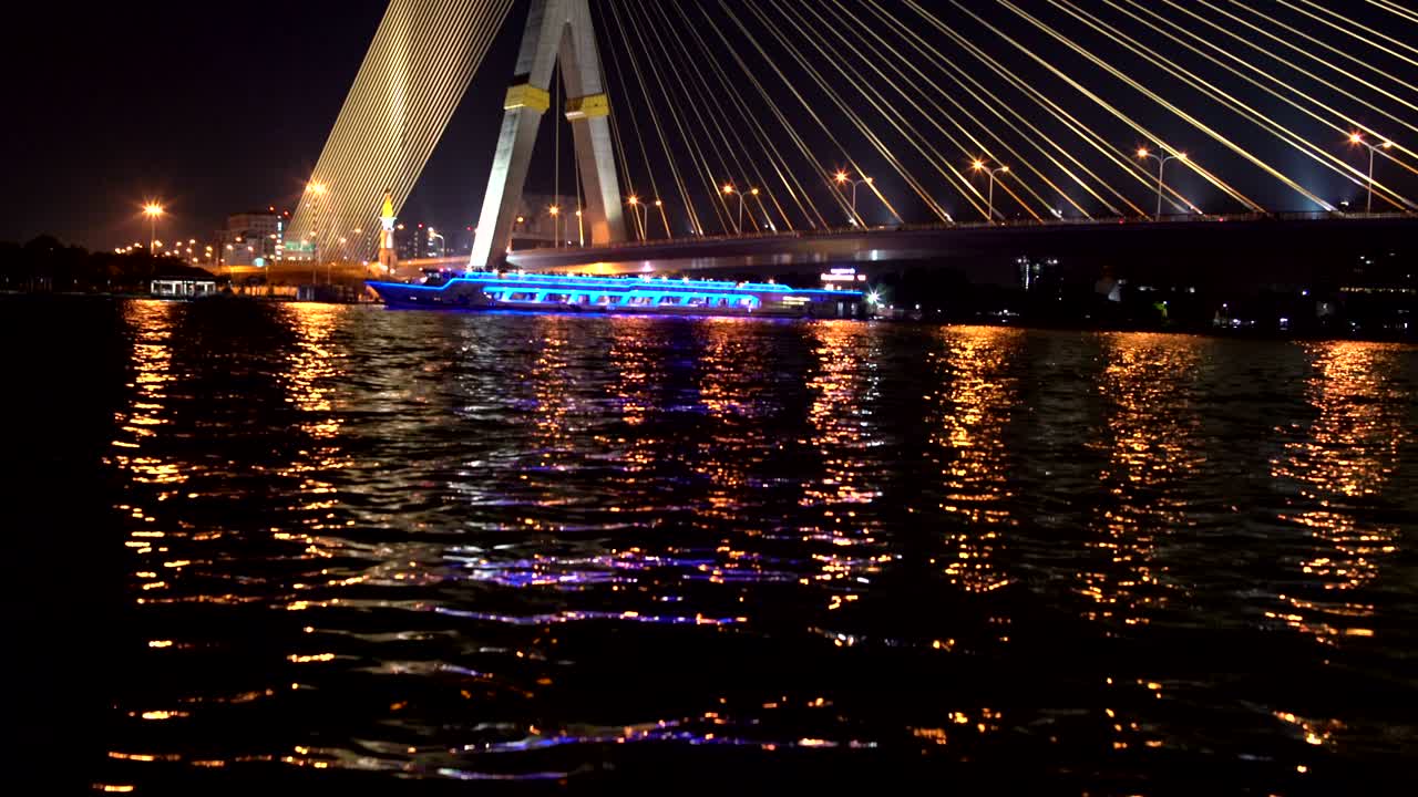 en el río bajo el puente de cable hay un barco con iluminación