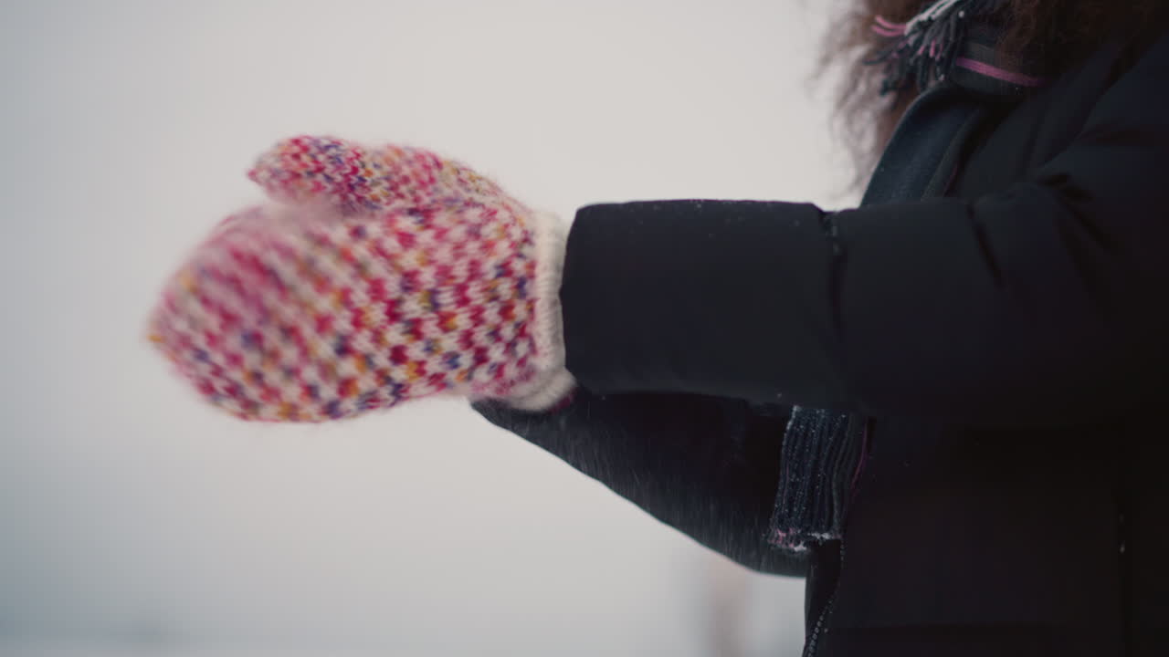 Closeup of colorful knitted mittens clapping together in cold outdoor winter setting, snowflakes scattering, cozy seasonal moment showing warmth, comfort, handmade texture winter lifestyle
