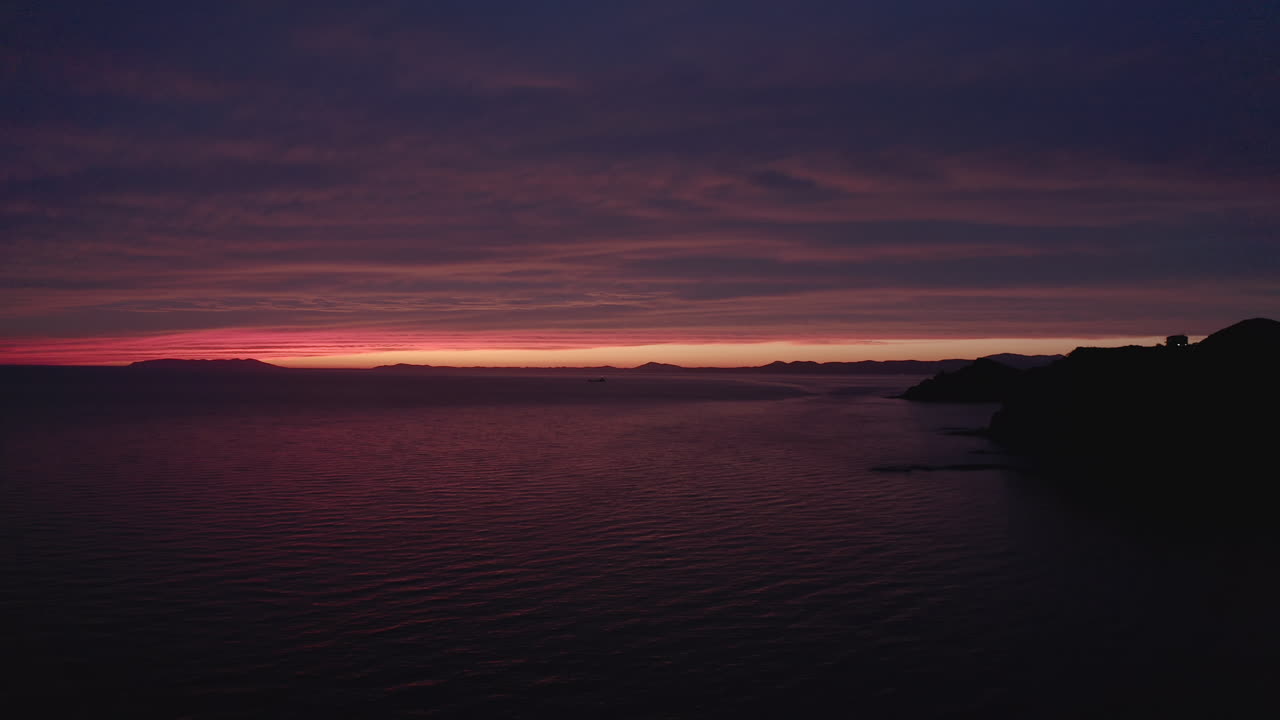 puesta de sol épica y colorida con una franja estrecha de cielo despejado a una distancia muy lejana y varios tonos de color rojo reflejados en la gran nube y la superficie del mar