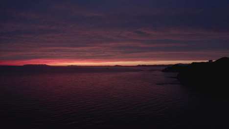 Episch-Farbenfroher-Sonnenuntergang-Mit-Einem-Schmalen-Streifen-Klaren-Himmels-In-Sehr-Weiter-Entfernung-Und-Verschiedenen-Rottönen,-Die-Sich-Auf-Der-Großen-Wolken--Und-Meeresoberfläche-Widerspiegeln